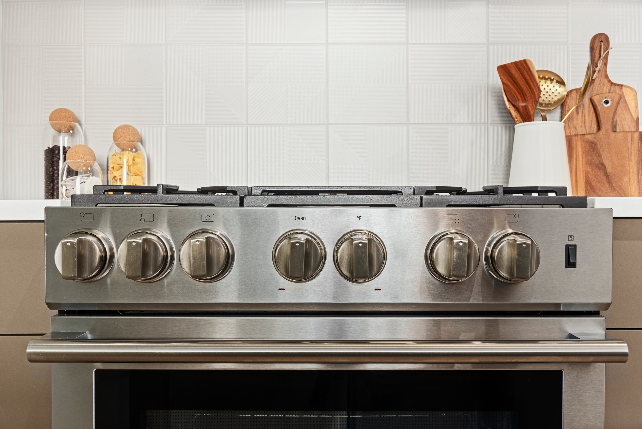 Detail of stainless steel stove oven knobs with white tile backsplash