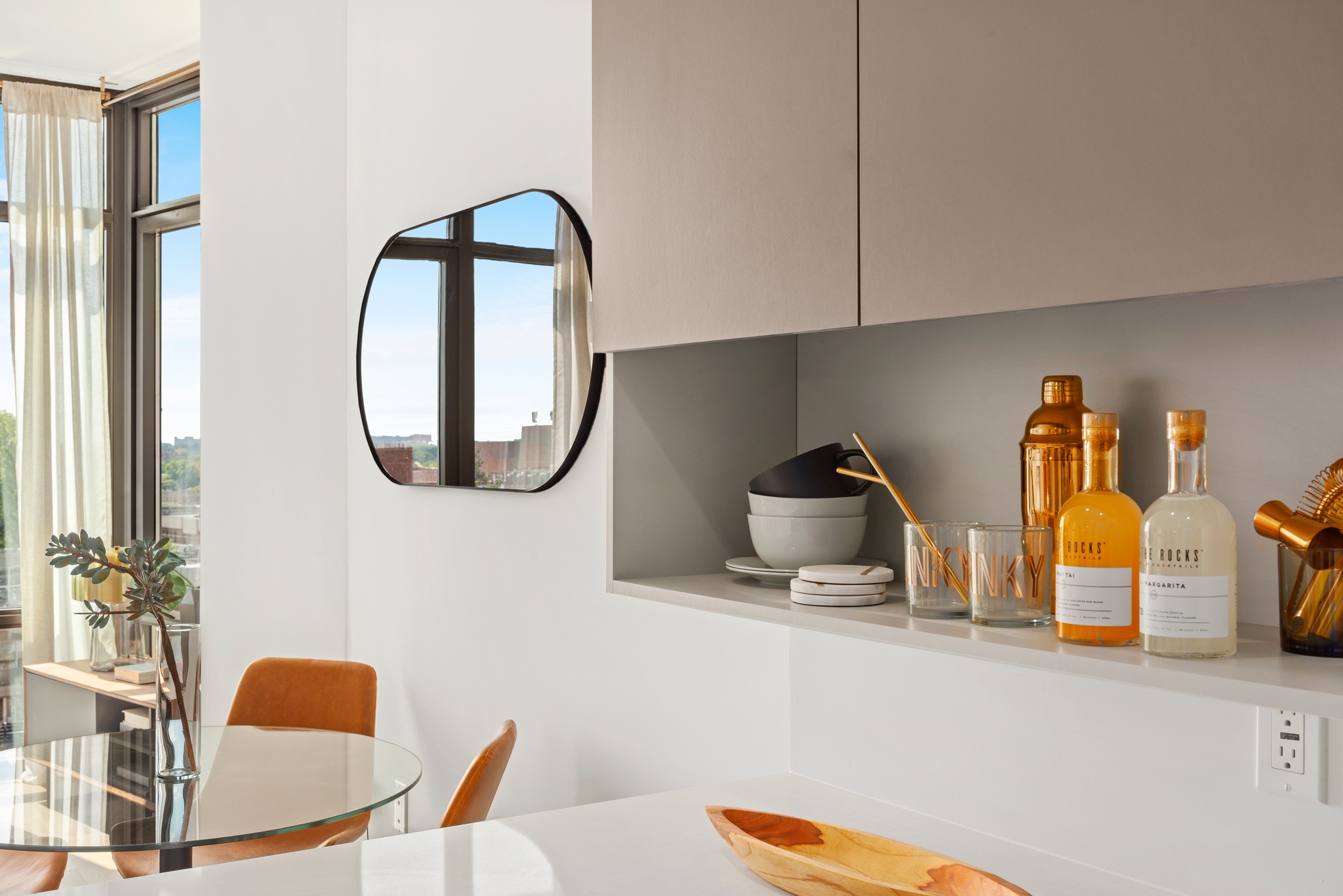 Kitchen detail showing built in shelf under tan cabinetry and glass table eat in seating with mirror above