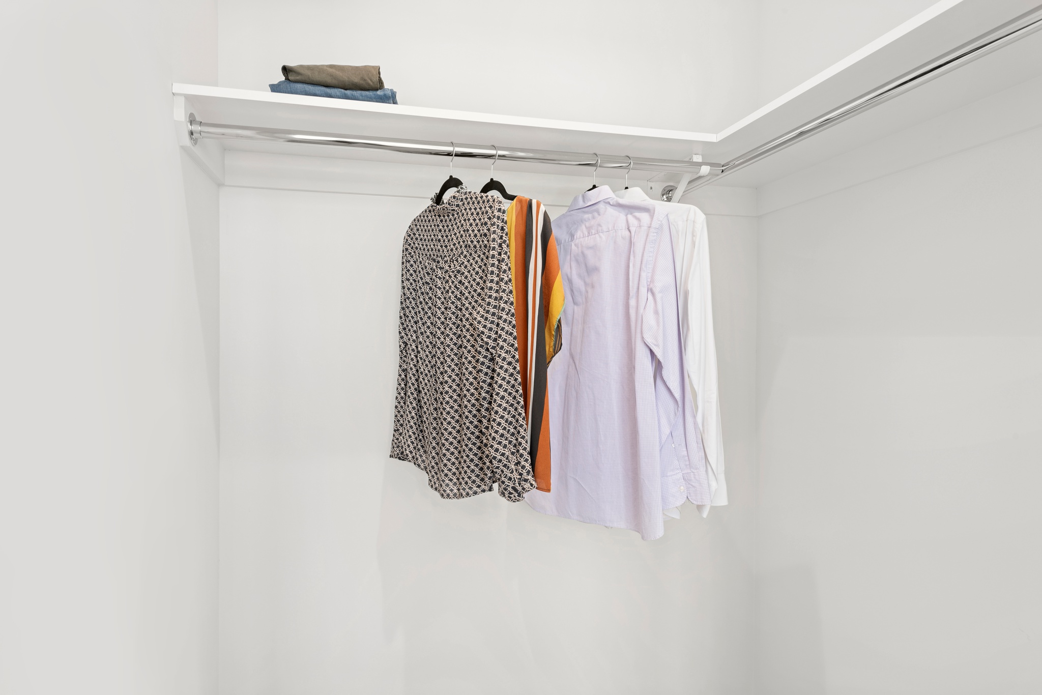 Spacious white closet with hanging bars with shirts hung and shelves above