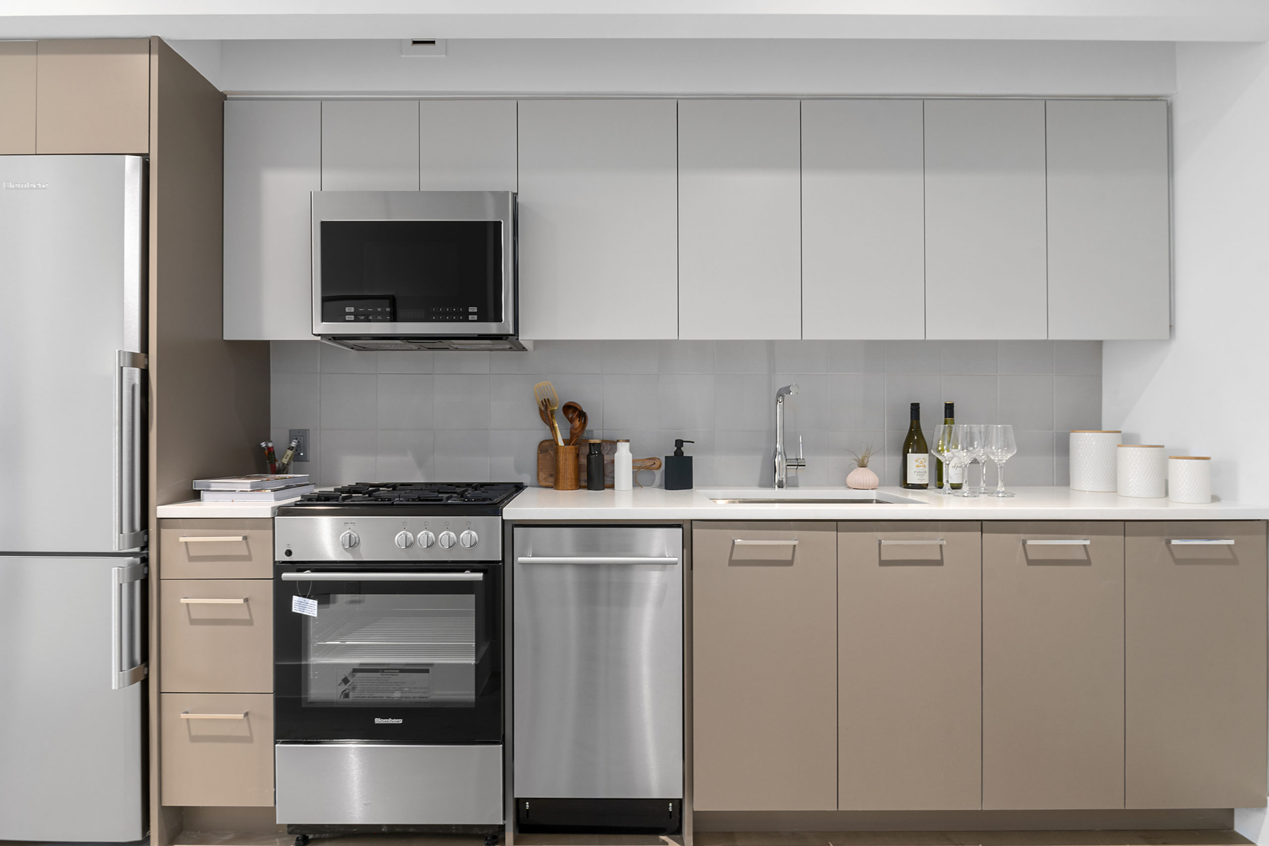 Modern kitchen with light grey and tan cabinetry, white counters, stainlless steel fridge, microwave, stove and dishwasher